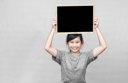 Little asian girl holding blackboard isolated on gray background.の写真素材
