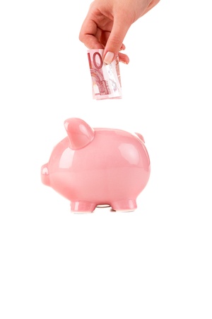 Female hand putting a coin into piggy bankの写真素材