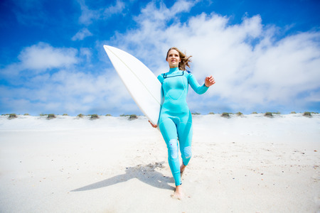 Surfer girl running at the beach with her surfboardの写真素材