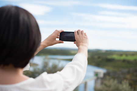 Back view of a woman taking photograph with a smart phone cameraの写真素材
