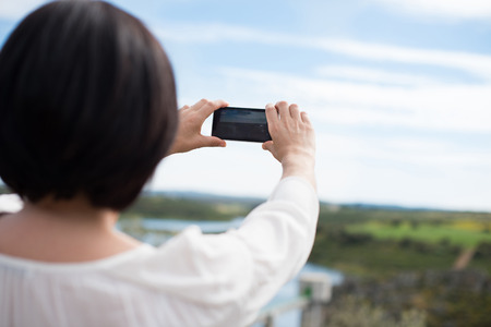 Back view of a woman taking photograph with a smart phone cameraの写真素材