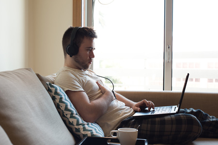 Man sitting on sofa with headphones and laptopの写真素材