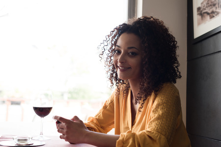 Afro woman typing on smartphone in restaurant