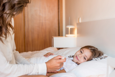 Mother taking care of her sick daughter in bedroomの写真素材