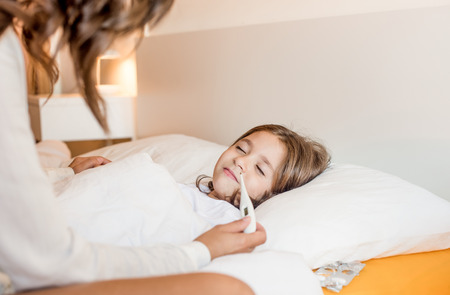 Mother taking care of her sick daughter in bedroomの写真素材