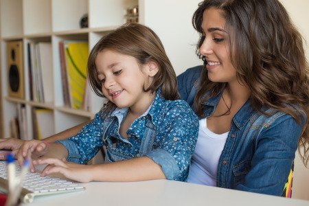 Young woman with little girl using computer at homeの写真素材