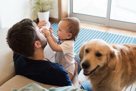 Family having fun with a feeding bottle - Father, baby and dog!の写真素材