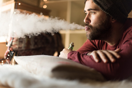 Young man with a knit cap using a vaperの写真素材