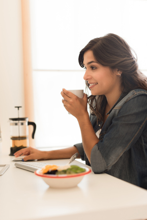 Young woman having breakfast on the computer deskの写真素材