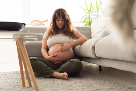 Happy pregnant woman sitting and touching her belly at homeの写真素材