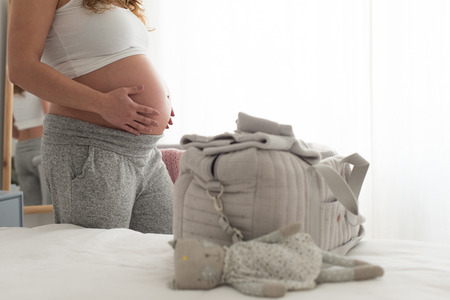 Happy pregnant woman sitting and touching her belly at homeの写真素材