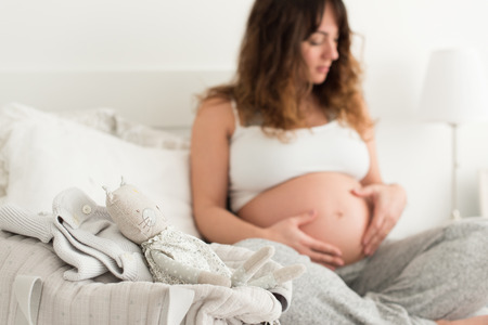 Happy pregnant woman sitting and touching her belly at homeの写真素材