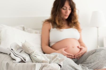 Happy pregnant woman sitting and touching her belly at homeの写真素材