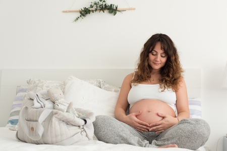 Happy pregnant woman sitting and touching her belly at homeの写真素材
