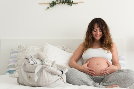 Happy pregnant woman sitting and touching her belly at homeの写真素材