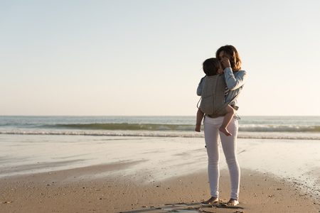 Mother with ergobaby carrying toddler on the beachの写真素材