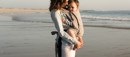 Mother with ergobaby carrying toddler on the beachの写真素材