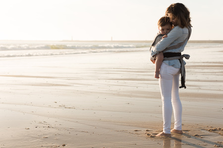 Mother with ergobaby carrying toddler on the beachの写真素材