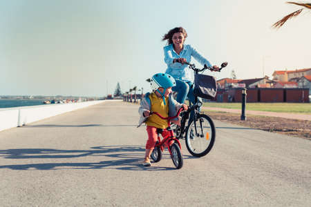 Little kid riding a balance bike with his mother on a bicycle in a city parkの写真素材