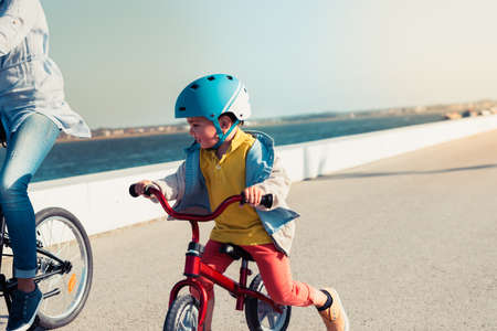 Little kid riding a balance bike with his mother on a bicycle in a city parkの写真素材