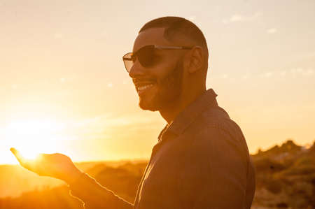 Happy latin man walking and enjoying the sunset with a natural landscape view. Warm natural light.の写真素材