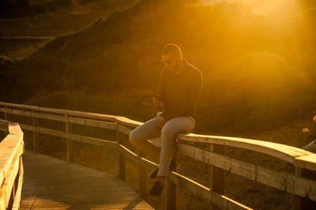 Latin man texting with a smartphone over an amazing sunset landscape view. Natural  outdoor lightの写真素材