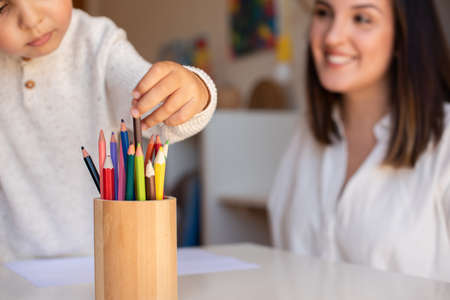 Little preschooler kid drawing with coloured pencils with mother or teacher educator. Focus on the pencils. Homeschooling. Learning community. Montessori school.の写真素材