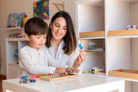 Lillte Kid playing with a tetris wood puzzle and mother or teacher help. Homeshooling. Learning Community. Montessori Schoolの写真素材