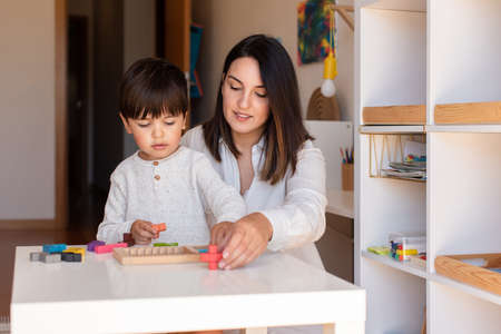 Lillte Kid playing with a tetris wood puzzle and mother or teacher help. Homeshooling. Learning Community. Montessori Schoolの写真素材