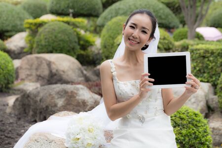 Asian bride holding and show digital tablet with a copy space, feeling so happinessの写真素材