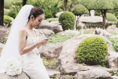 Beautiful Attractive Asian bride smile and talking with her friend in smartphone in wedding day feeling so proud and happinessの写真素材