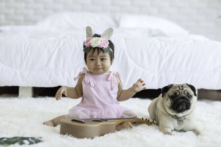 Cute Sweet Adorable Asian Baby wearing pink dress Sitting on white carpet Crying with dog pug breed Friendly in cozy bedroom,Dog with Baby Conceptの写真素材