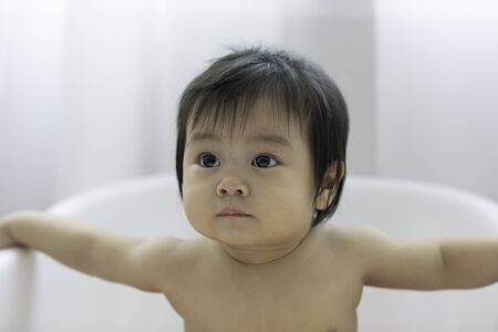Cute Sweet Adorable Asian Baby Sitting on bathtub with plastic balls smiling and playing with...
