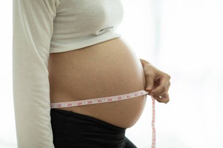 Close up pregnant woman measuring her belly with measuring tape,Healthy pregnancy concept,Selective...