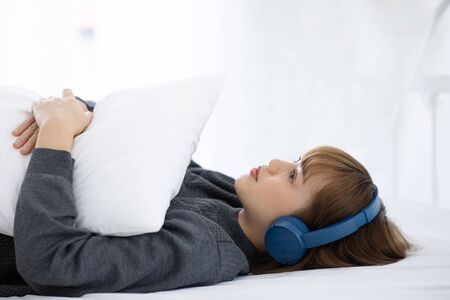 Beautiful Attractive Asian young woman listen music and lying on bed in bedroom feeling so relax and...