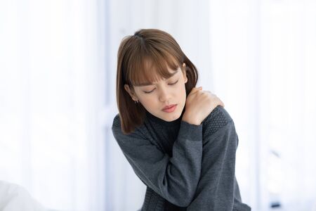 young Asian woman sitting on bed has neck pain after wake up in the morning,Healthcare Conceptの写真素材