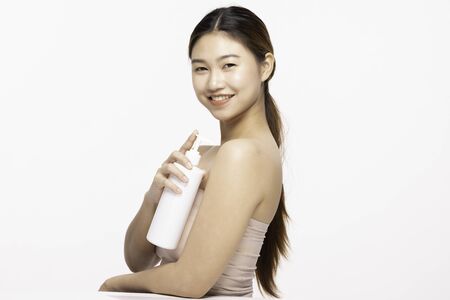 Attractive Asian young woman smile with white teeth holding white Lotion bottle feeling so happy and cheerful with healthy Clean and Fresh skin,isolated on white background,Beauty Cosmetology Conceptの写真素材