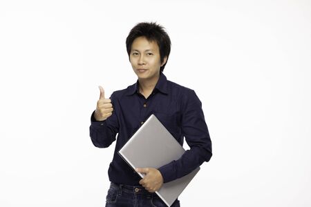 Asian Handsome man wearing casual blue shirt standing and holding Computer laptop and showing thumbs up with confident and happiness emotional,Isolated on white background,Asian man Conceptの写真素材