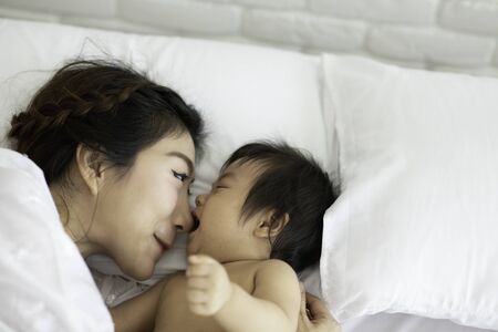 Happy Beauty mother Holding Cute Sweet Adorable Asian Baby wearing white dress smiling and playing...