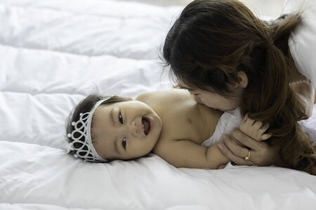 Happy Beauty mother Holding Cute Sweet Adorable Asian Baby wearing white dress smiling and playing...