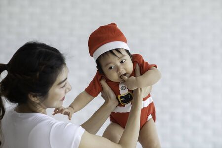 Happy Beauty mother Holding Cute Sweet Adorable Asian Baby wearing white dress smiling and playing...