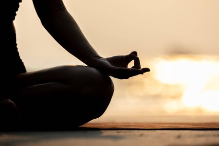 Silhouette Close up hand of woman practice yoga meditation lotus pose on the beach in thailand,Feeling so comfortable and relax in holiday with golden light,Healthy Concept,warm toneの写真素材