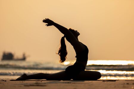 Silhouette Happy Asian woman wearing black sport wear practice yoga Pigeon pose on the beach with beautiful sea in Tropical island,Feeling comfortable and relax in holiday,Vacations Conceptの写真素材