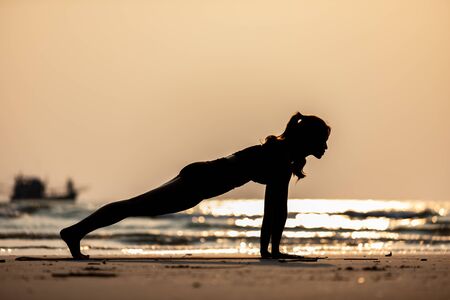 Silhouette of Asian woman practice yoga Plank or Phalakasana Pose on the sand and beach with sunset beautiful sea in Tropical island,Feeling comfortable and relax in holiday,Vacations Yoga Conceptの写真素材