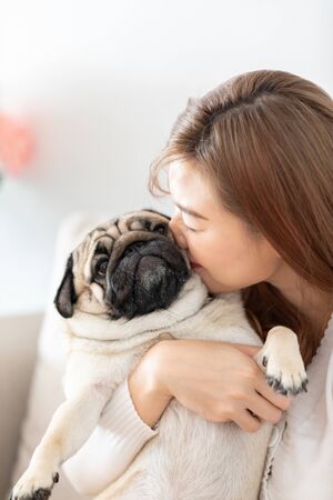 Beautiful Attractive Asian woman kissing her Cute dog pug breed with boring and funny face on bed feeling so sweet and lovely, Friendly Conceptの写真素材