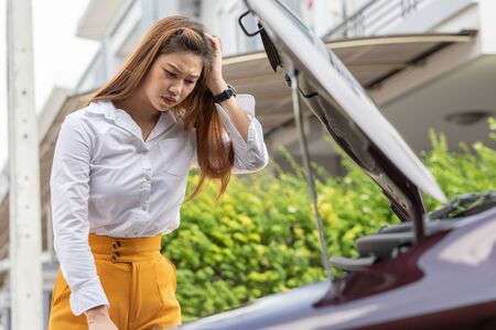 Asian young woman open car hood looking car engine after found car problem and accident with her car broken on the road during the tripの写真素材