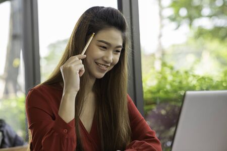 Beautiful Attractive Asian woman wearing red dress working with computer laptop and thinking to get ideas and requirement in Business startup feeling so happiness,Business Startup Conceptの写真素材