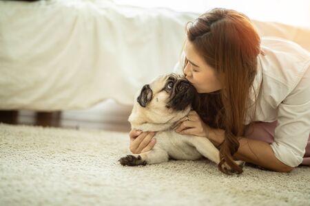 Beautiful Attractive Asian woman kissing her Cute dog pug breed with boring and funny face on bed feeling so sweet and lovely,Friendly Conceptの写真素材