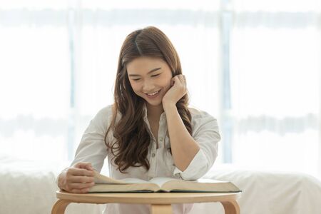 Beautiful Attractive Asian woman sitting on bed in bedroom reading book for learn and education smile and positive thinking feeling so happiness and comfortable,Education Conceptの写真素材