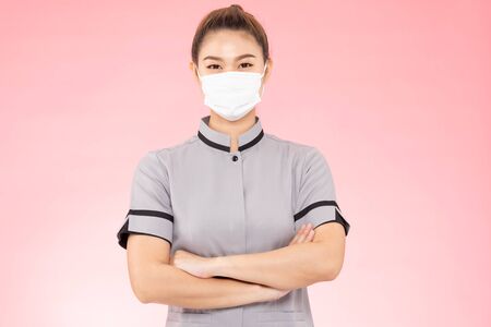 Attractive Beautiful Asian woman maid wearing face mask smile and cross arm feeling so happiness and confident,Isolated on pink background,Cleaning Service conceptの写真素材